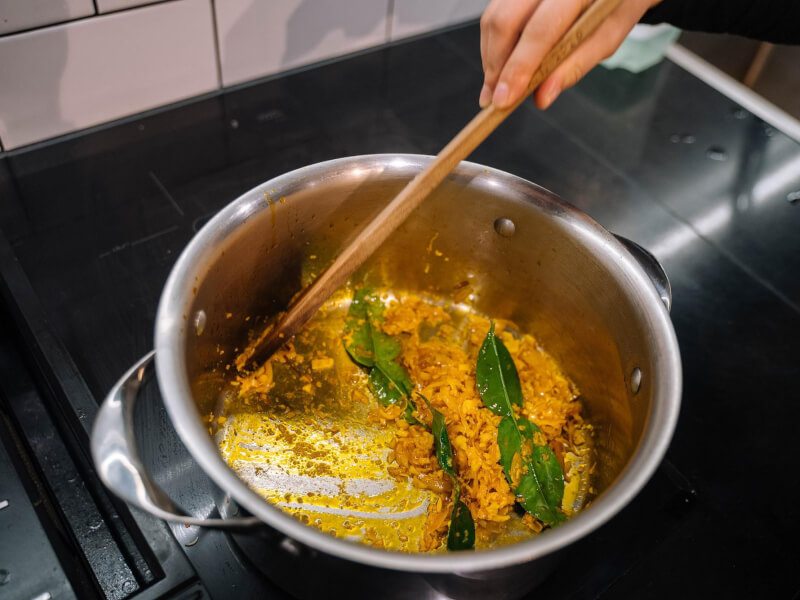 Using a wooden spoon to bloom spices in a metal saucepan